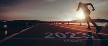 New Year 2023 Or Start Straight Concept.word 2023 Written On The Asphalt Road And Male Runners Are Starting To Run Ready For New Year At Sunset.Concept Of Challenge Or Career Path And Change.