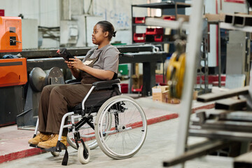 African worker with disability sitting in wheelchair and working at machine with remote control