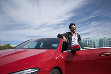 Handsome Young Man With Beard, Sunglasses, Leather Jacket And White Shirt, Leaning On The Roof Of His Red Sports Car, Very Smiling. Concept Beauty, Fashion, Trend, Luxury, Motor, Sports.