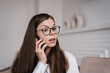 Anxious brunette hispanic young woman in white shirt, glasses, talking by phone in concern mood. Pretty Caucasian businesswoman discusses troubles with manager trying to resolve problem. Finance