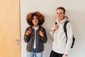 Two students standing together at wall and looking at camera