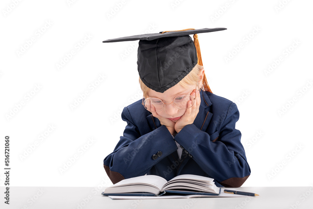 Bored boy in school uniform and students hat sits at table and reads ...