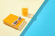 Creative summer scene with orange book, stylish white sunglasses and crystal glass on sunny blue and sandy background. Leisure by the pool idea.