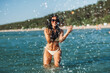 © Syda Productions - people, summer and swimwear concept - happy smiling woman in bikini swimsuit splashing sea water on beach