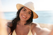 © Syda Productions - people, summer and swimwear concept - happy smiling young woman in bikini swimsuit and straw hat taking selfie on beach