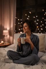 Wall Mural - people, bedtime and rest concept - happy smiling woman in pajamas with coffee sitting in bed at night