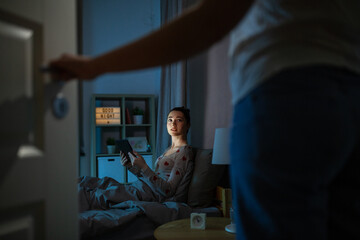 Wall Mural - technology, bedtime and people concept - teenage girl with tablet pc computer sitting in bed at home at night and mother entering room