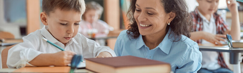 Happy kind teacher is helping a boy in elementary school lessons.