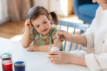 Poster - holidays, family and people concept - happy mother and little baby daughter dyeing easter eggs with colors at home