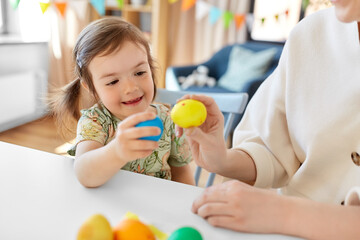 Poster - holidays, family and people concept - happy little baby daughter and mother tapping colored easter eggs at home