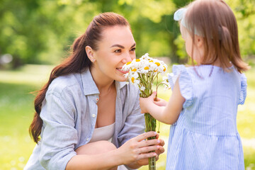 family, motherhood and people concept - happy mother with little daughter with chamomile flowers at summer park or garden