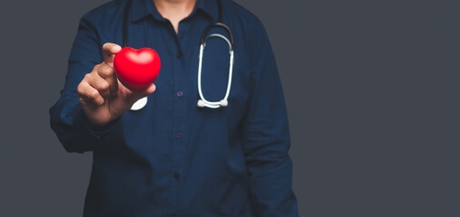 Close-up of hand doctor holding a red heart shape while standing on gray background