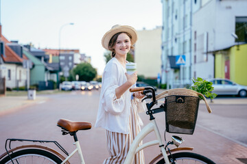 Young woman with reusable coffee mug crossing road with retro bicycle outdoor. Slow living, simple village eco life.