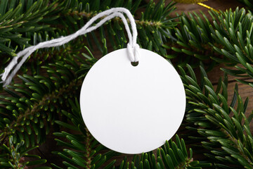 Christmas round white tag mockup with white cord, close up on natural fir tree branch, with cones and Christmas decoration, Christmas sale concept. Blank paper circle laber product tag mockup