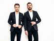 © halayalex - Portrait of two handsome confident stylish hipster lambersexual models. Sexy modern men dressed in black elegant suit. Fashion male posing in studio near white wall