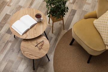 Wooden nesting tables near houseplant and armchair in room. Interior design