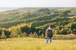 © Lyubov - Tourist with backpack standing on top of hill in grass field and enjoying beautiful landscape view. Rear view of teenage boy hiker resting in nature. Active lifestyle. Concept of local travel