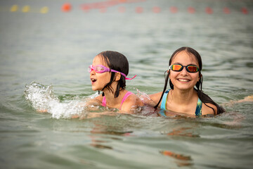 Wall Mural - Girls sisters swimming together in water and smiling in summer