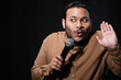emotional indian stand up comedian showing stop gesture while telling jokes into microphone isolated on black.
