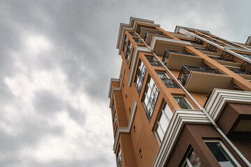 A yellow multi-storey building against a blue cloudy sky. Modern residential building with balconies and windows in a residential complex. Street photography. A yellow house against the sky.