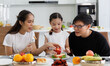 © atitaph - A happy Asian family spends lunch, vegetables, fruit, and dates at the table in their home. Cute little daughter having fun talking. Father, mother