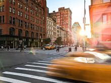 Blurred Yellow Taxis Driving Through The Intersection Of 23rd Street And 5th Avenue In New York City With Sunlight Background