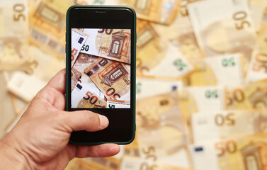 man hand takes a picture of euro banknotes on smartphone. Money paper 50 euro banknotes on the background of a smartphone screen, the concept of business, investment and income growth.