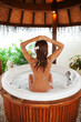 Beautiful tanned woman relaxing in jacuzzi. Body, skin and hair care, spa. Sexy lady sitting at bath with spume.