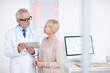 © Mediaphotos - High-qualified senior gray-haired doctor in eyeglasses and lab coat standing in clinic room and counseling mature female patient
