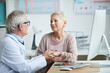 © Mediaphotos - Senior doctor in eyeglasses sitting at table and holding hand of mature female patient while giving hope and comfort to her