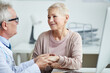 © Mediaphotos - Professional male practitioner sitting at table and touching hands of female patient while supporting her