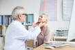 © Mediaphotos - Serious senior male oncologist with gray hair sitting in front of mature female patient and touching her neck during checkups