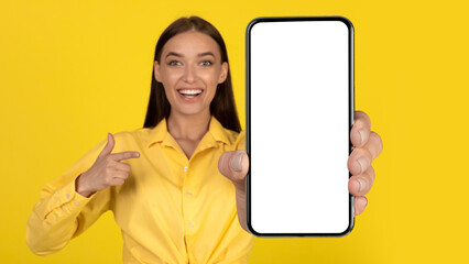 Cheerful Female Holding Cellphone Showing Blank Screen Over Yellow Background