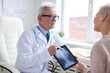 © Mediaphotos - Confident senior male doctor in lab coat using digital tablet while telling patient about spinal cord disorder