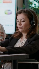 Wall Mural - Vertical video: Woman with physical disability working at call center with audio headset and microphone to help clients. Telemarketing operator using headphones to chat at helpline care service