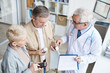 © Mediaphotos - Serious senior male doctor with white hair standing in clinic and giving pills for senior couple