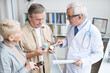 © Mediaphotos - Serious aged male doctor in glasses standing in clinic and explaining senior couple how to take medicine correctly