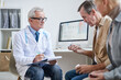 © Mediaphotos - Serious senior male doctor in glasses making notes in clipboard while prescribing medication for mature patients