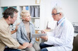 © Mediaphotos - Serious high-qualified cancer doctor in glasses showing medical records on tablet and giving advice to mature woman with serious disease, her husband holding her hand as symbol of support