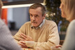 © Mediaphotos - Wrinkled aged man in beige sweater sitting at table and drinking tea while sharing stories with friends
