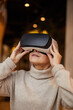 © Mediaphotos - Smiling mature woman in turtleneck sweater holding virtual reality glasses while watching 3D video