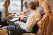 © Mediaphotos - Mature man in wheelchair pushed by wife joining friends in cafe, group of seniors drinking tea in background