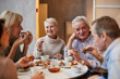 © Mediaphotos - Group of positive aged friends sitting at table and laughing while drinking tea and eating pizza together in cafe