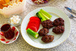 Portion of just cooked Turkish grilled meatballs, inegol kofte, served on plate with vegetables.