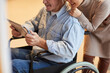 © Mediaphotos - Close-up of positive aged couple watching video on digital tablet: smiling woman leaning on wheelchair of husband