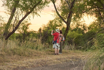 Wall Mural - Couple of mature travelers taking pictures and enjoying the scenery at sunset at the Multiple Uses Natural Area, River of the Birds Park, Parque Rio de los Pajaros, in Colon, Entre Rios, Argentina.