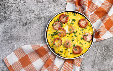 Wall Mural - Omelet with herbs and sausage on a round plate on a dark grey background. Top view, flat lay