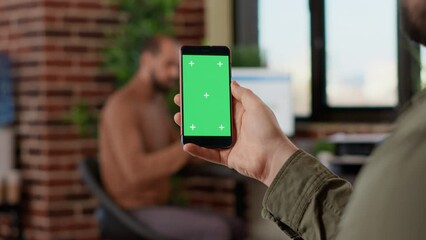 Startup worker using isolated greenscreen on mobile phone, looking at blank mockup display with copyspace background. Analyzing chroma key template on modern smartphone display.