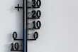 Classic black analog thermometer hanging on white wall displaying blue temperature scale of ten, 10 degrees celsius