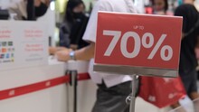 Red Sign With A 70 Percent Discount To Attract Customers. In The Background In Blur, Unrecognizable Customers At The Checkout Are Eager To Buy At A Bargain Price In The Store. Discount Concept.